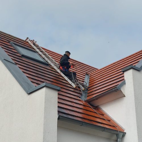 Person wäscht Dach mit Hochdruckreiniger